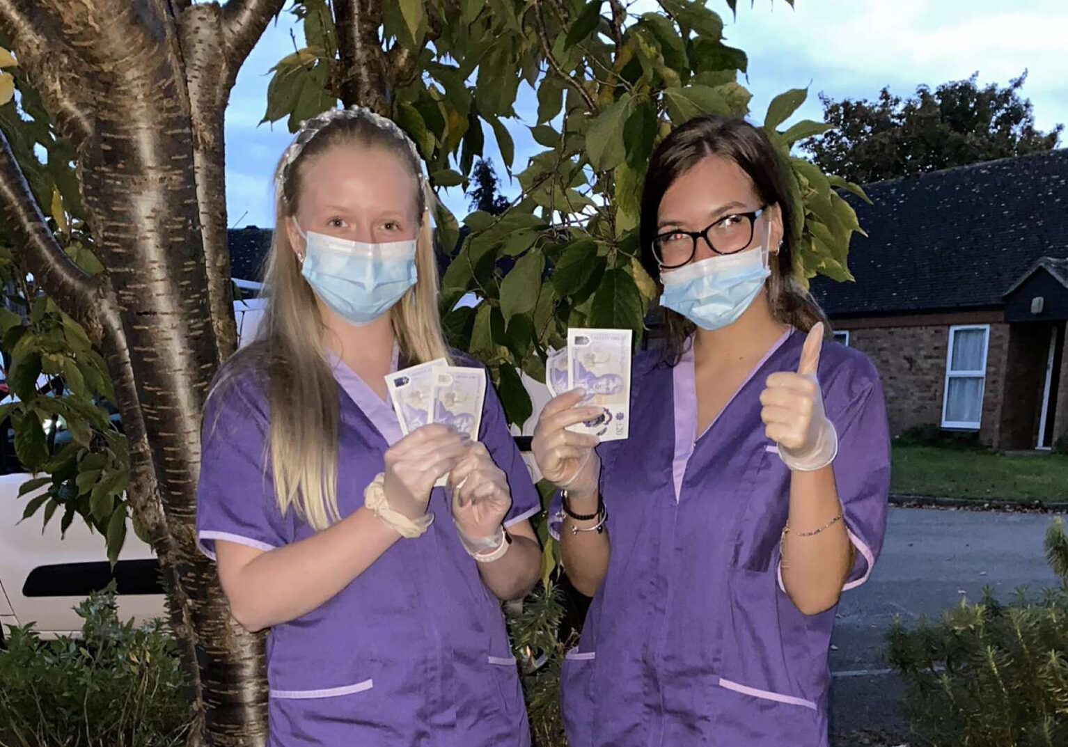 Two nurses in purple scrubs holding up their hands.