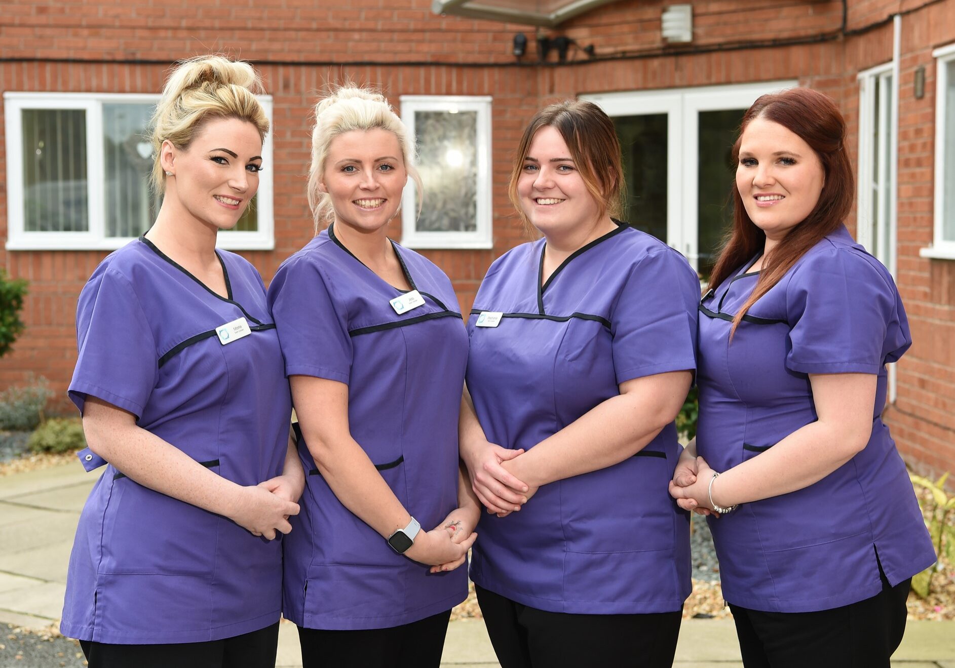 Four women in purple scrubs standing next to each other.