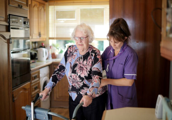 A woman helping an older person use a walker.